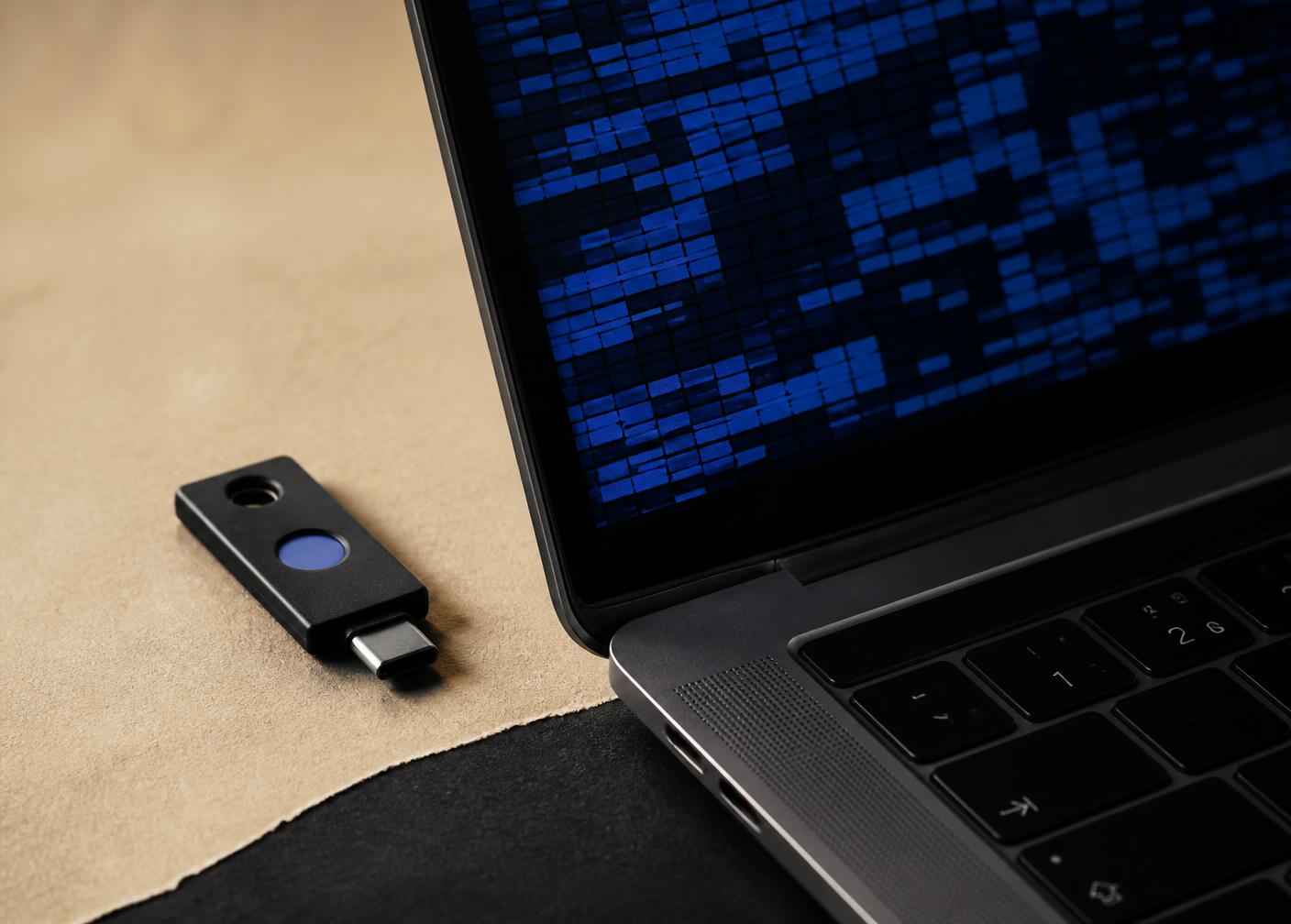 Hardware security key beside a laptop displaying abstract blue encrypted data